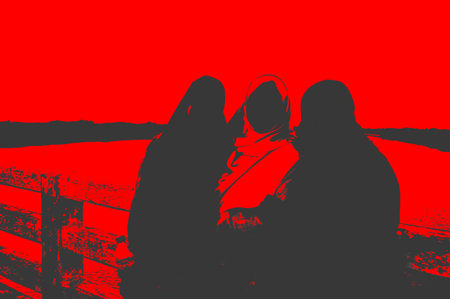Silhouette of two young women sitting on a wooden fence.