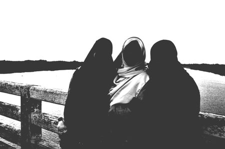 Muslim women sitting on the bench and looking at the sunset. Black and white.
