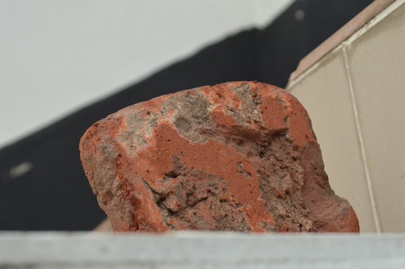 A detailed close-up captures the texture and imperfections of a weathered red brick against a...