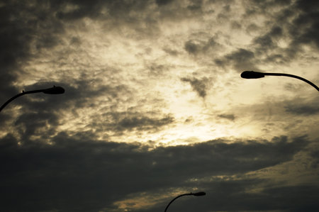 Silhouette of street lights on the background of the cloudy skyの写真素材