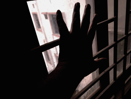 Silhouette of a man's hand behind the bars of a window
