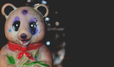 A plastic toy panda figurine sits on a polished wooden table with soft bokeh from a water bottle in...