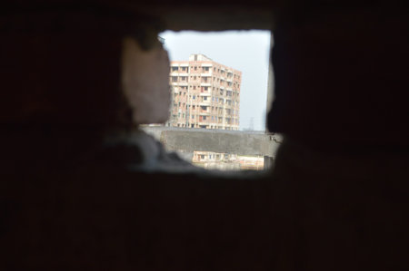 Close-up view of a weathered red brick wall with an irregular hole and rough mortar, dust and grit...
