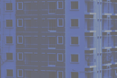 Blue-tinted photograph of an urban apartment building facade showing repeating windows, metal...