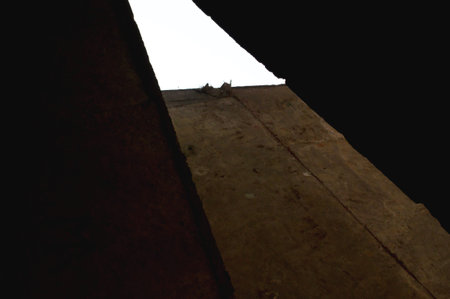 Moody architectural detail of a cracked concrete beam illuminated by a sliver of light inside an...