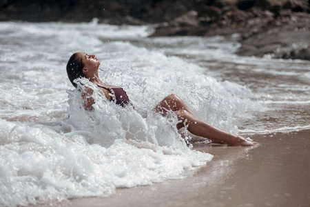 A tanned, young beauty bathes in the sea waves and closes her eyes. Holidaysの写真素材