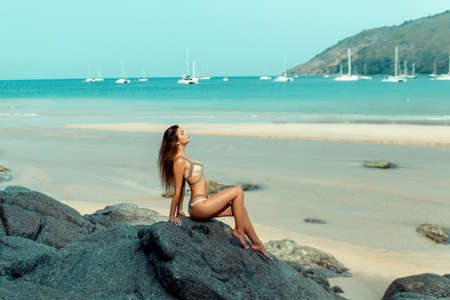 A woman is relaxing on a rock near the sea with more yachtsの写真素材