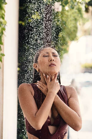 beautiful asian girl in a bikini taking a shower in a bungalow yard.