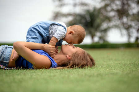 mom and her little smiling son play together, lying on the lawn
