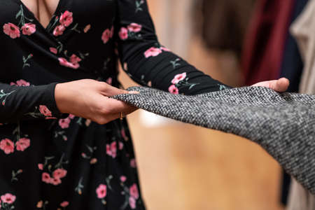 Young girl in a short black dress in a pink flower posing holding a gray sleeve from a sweater....