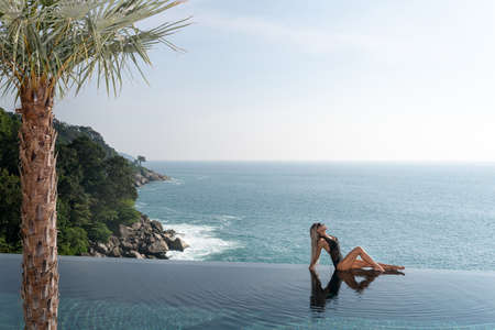Slender beautiful blonde relaxes in the infinity pool at the resort