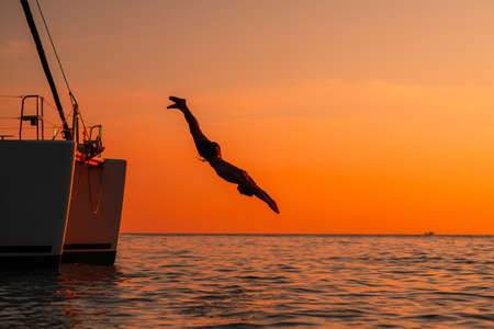 Young man jumping off yacht into water ocean at sunset.の写真素材