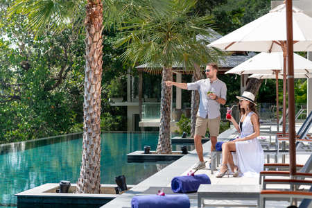 Couple tasting tropical drinks while sitting on sun loungerの写真素材