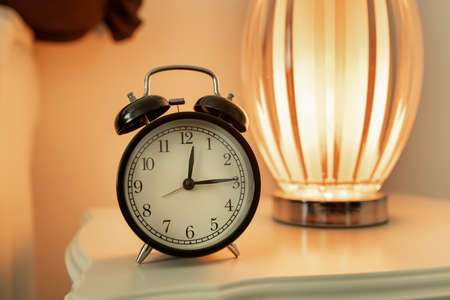 Old vintage black alarm clock located close-up on a white bedside table