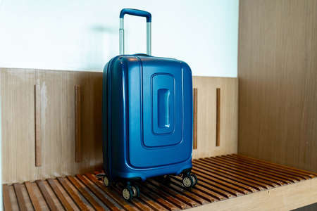 Blue suitcase in light hotel room with brown wooden details.の写真素材