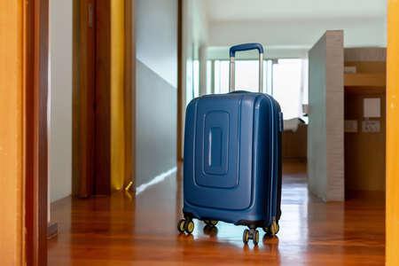 Blue suitcase in light hotel room with brown wooden details.の写真素材