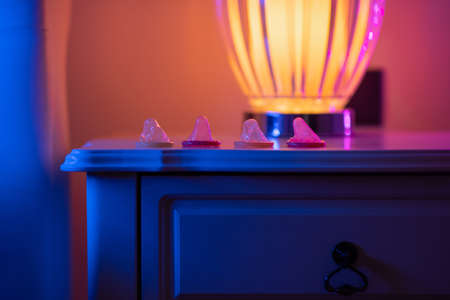 A pile of condoms open, lie on a bedside wooden table near the lamp.