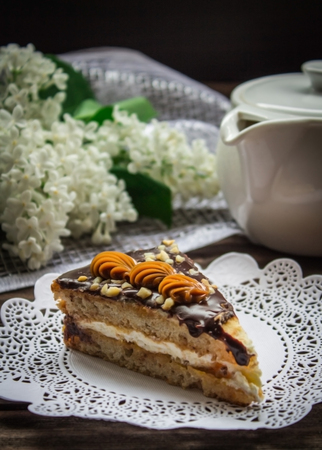 Piece of cake, teapot and lilac on a brown wooden background.