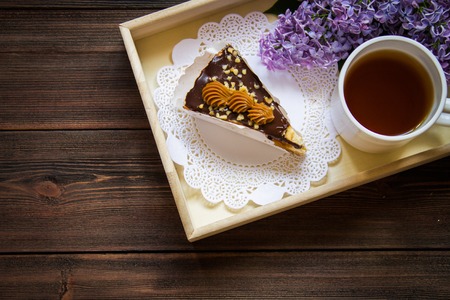 Piece of cake, cup of tea and lilac in a tray on a brown wooden backgroundの写真素材