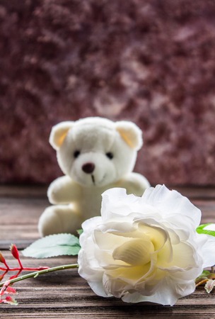 White teddy bear with a rose on wooden table, brown background.の写真素材
