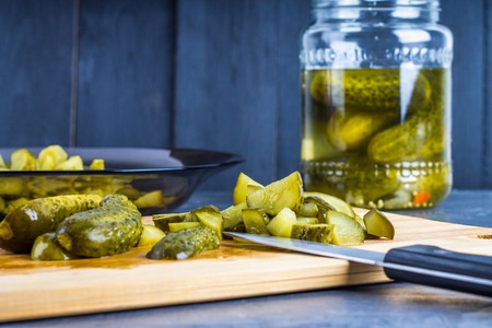 Cucumbers or pickled gherkins with a knife on a wooden cutting board. Blue gray background. Bank...