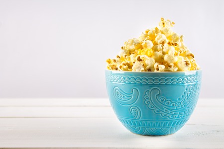 Salty popcorn in a blue cup is on a wooden tableの写真素材