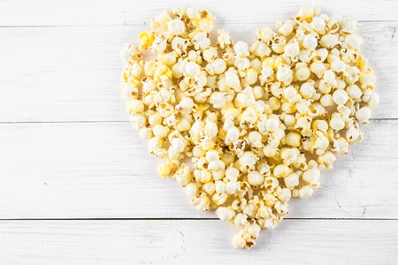 Salted popcorn in the shape of heart on a white table. Top viewの写真素材