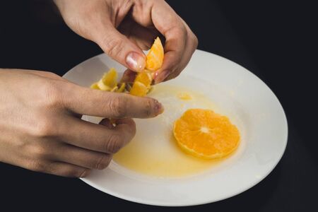 The girl is eating an orange. Hands holding orange slicesの写真素材