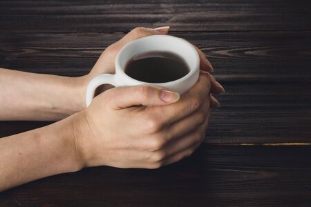 Woman hands holding cup of coffee on wooden table.の写真素材