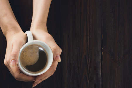 Woman hands holding cup of coffee on wooden table.の写真素材