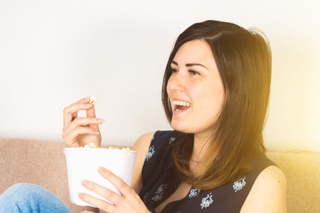 A girl on the couch watching TV and eating popcorn.の写真素材