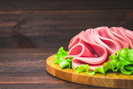 Sliced sausage with salad on a round wooden boardの写真素材