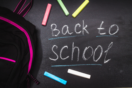 Back to school message on Blackboard inscribed with colorful chalk for background. Backpack