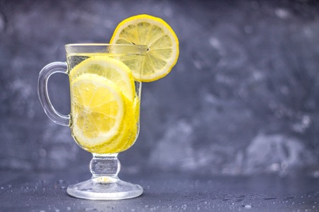 Homemade lemonade in a glass with a handle on a gray concrete background. Water with slices of lemon on a dark background.の写真素材