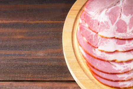 Sliced ham with fresh green lettuce leaves on a round cutting board. Meat products on a brown wooden table.の写真素材