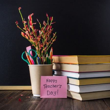 Concept of Teacher's Day. Objects on a chalkboard background. Books, green apple, plaque: Happy Teacher's Day, pencils and pens in a glass, sprig with autumn leaves.の写真素材