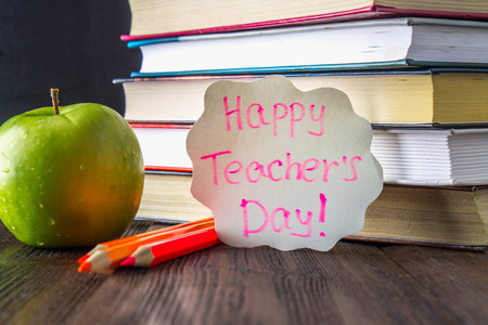Concept of Teacher's Day. Objects on a chalkboard background. Books, green apple, plaque: Happy Teacher's Day, pencils and pens in a glass, sprig with autumn leaves.の写真素材