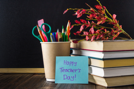 Concept of Teacher's Day. Objects on a chalkboard background. Books, green apple, plaque: Happy Teacher's Day, pencils and pens in a glass, sprig with autumn leaves.の写真素材