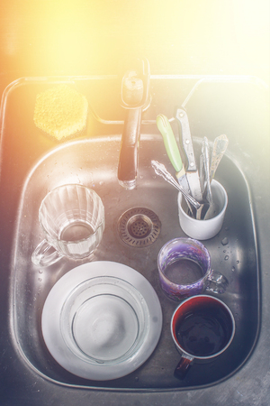 Dirty dishes in foam in the sink waiting for washing. Mugs, plates, cutlery.の写真素材