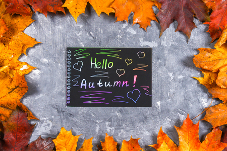 A frame of yellow and orange autumn maple leaves on gray dark concrete. Black plate with colored text. The inscription is hello autumnの写真素材