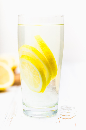 A glass beaker and a jug of cold lemonade on a white wooden background surrounded by lemonsの写真素材