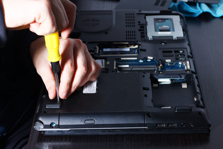 Closeup shot of male hands working on disassembling and cleaning circuit board in laptop using brushの写真素材