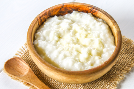 Rice milk porridge with nuts and raisins in wooden bowls on a white wooden tableの写真素材