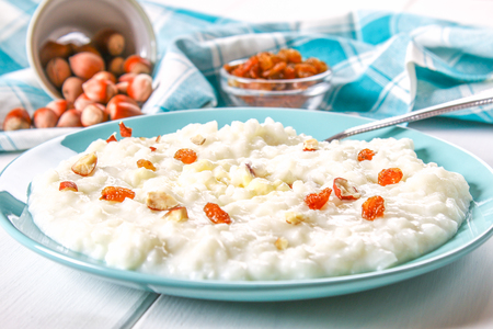Rice milk porridge with nuts and raisins in a blue dish on a white wooden tableの写真素材