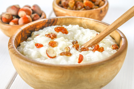 Rice milk porridge with nuts and raisins in wooden bowls on a white wooden tableの写真素材