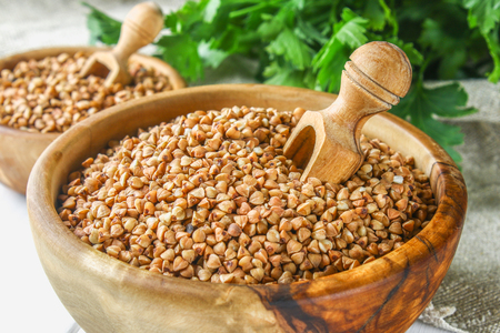 Raw buckwheat in wooden bowls and a scoop on sackcloth on a wooden background. Healthy diet foodの写真素材