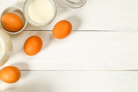 Raw brown chicken eggs, milk, sugar, flour, whisk, rolling pin on a white wooden table. Ingredients for cookingの写真素材