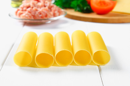 Italian pasta cannelloni. Raw tube for stuffing stuffing surrounded by ingredients for cooking,...