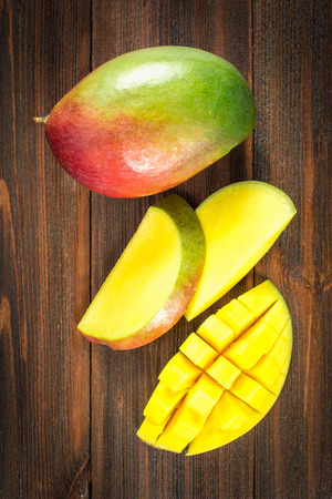 Tropical fruit mango on a wooden background, whole or slicedの写真素材