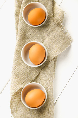 Raw brown chicken eggs in glass bowls on a white wooden table. Ingredients for cookingの写真素材